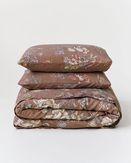 A stack of three bedding items, including two pillows and a folded duvet cover, in a brown floral pattern on a light gray background.